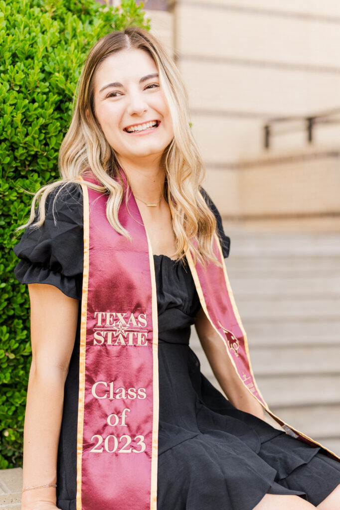 Texas State University senior smiling off camera in front of McCoy building. 